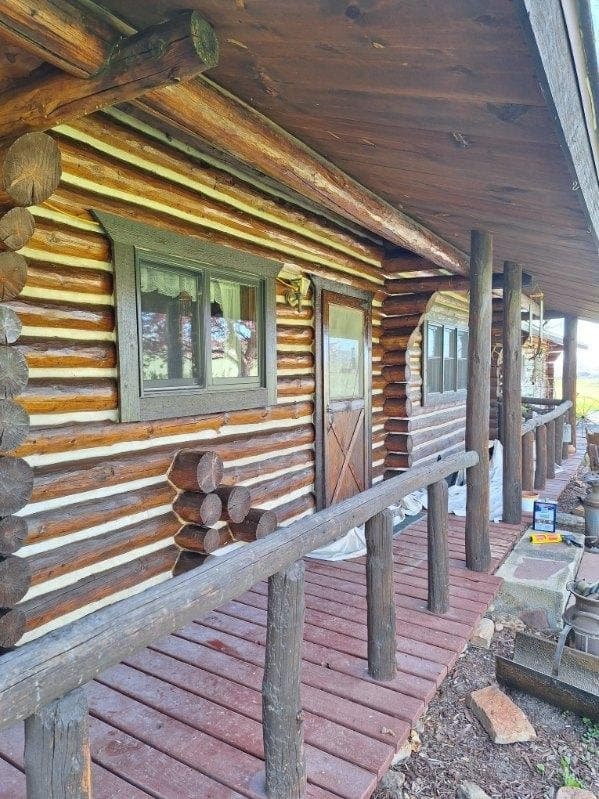 Log cabin exterior with wooden deck and green-trimmed windows